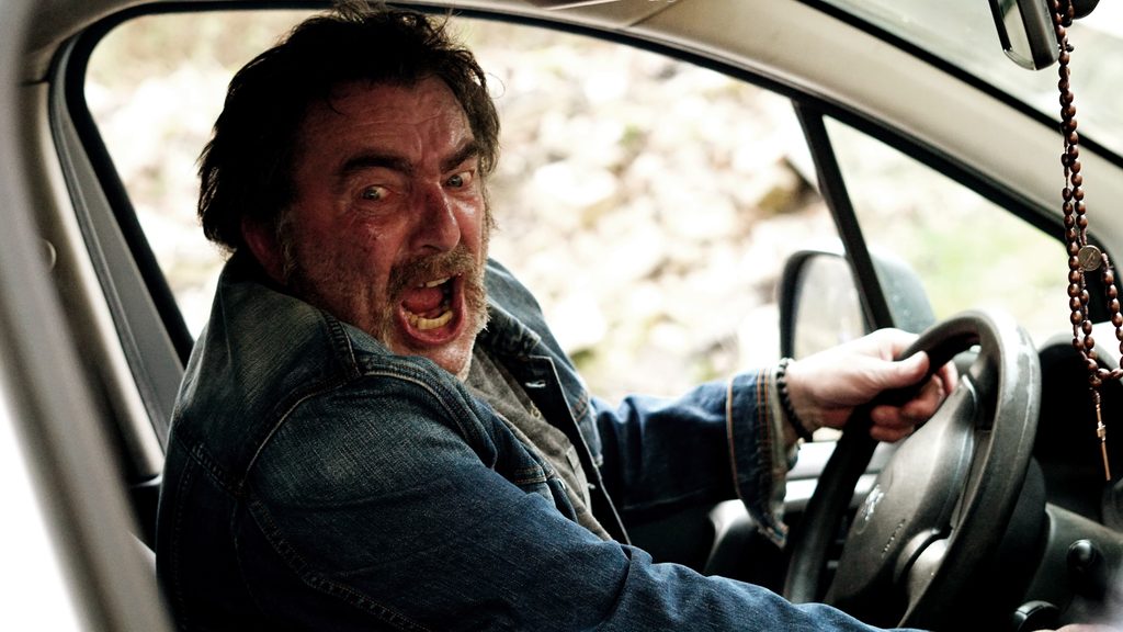 Un homme hurle au volant de sa voiture, un chapelet pendu au rétroviseur, dans Inferno, film belge de Brandon Gotto